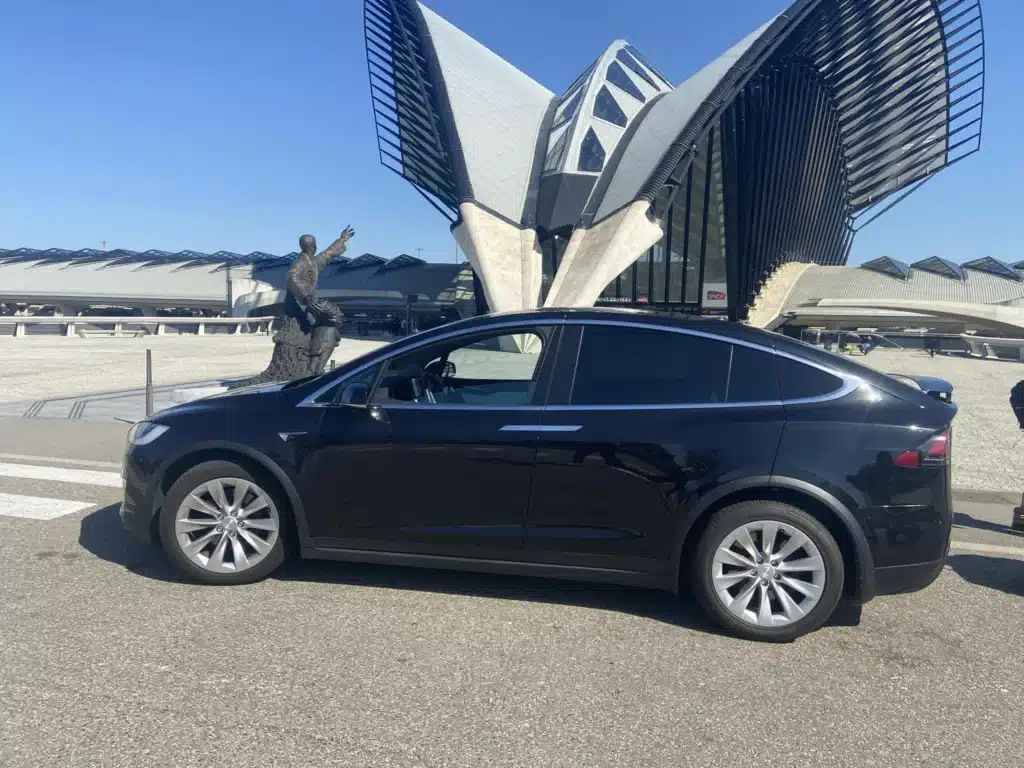 Tesla Model X noire à la Gare Lyon Saint-Exupéry TGV. Tesla Model X noire devant la spectaculaire architecture ailée de la Gare Lyon Saint-Exupéry TGV. Statue de l'aviateur.