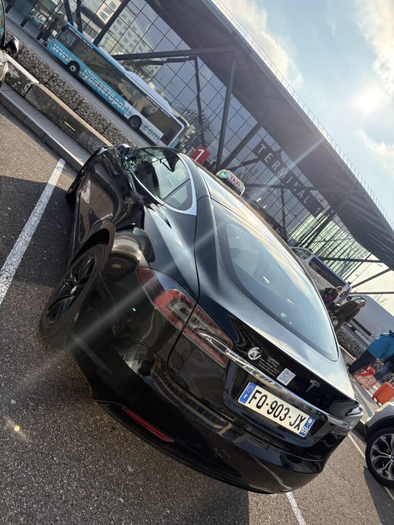 Tesla Taxi Model S à l'Aéroport Lyon Terminal 1 Tesla Model S taxi noir garé près du TERMINAL 1 de l'aéroport de Lyon par temps ensoleillé. Plaque FQ-903-JX. Feux taxi verts.